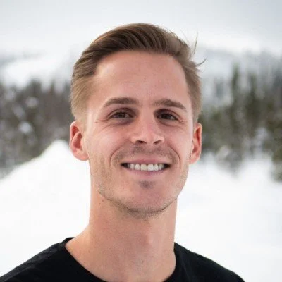 A young man smiling outdoors in a snowy landscape.
