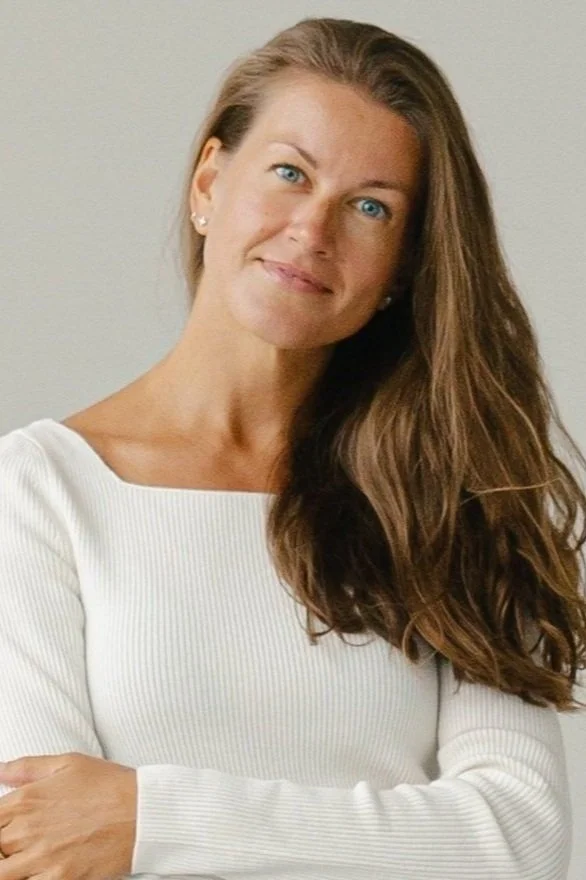 Woman with long brown hair wearing a white top, smiling at the camera.