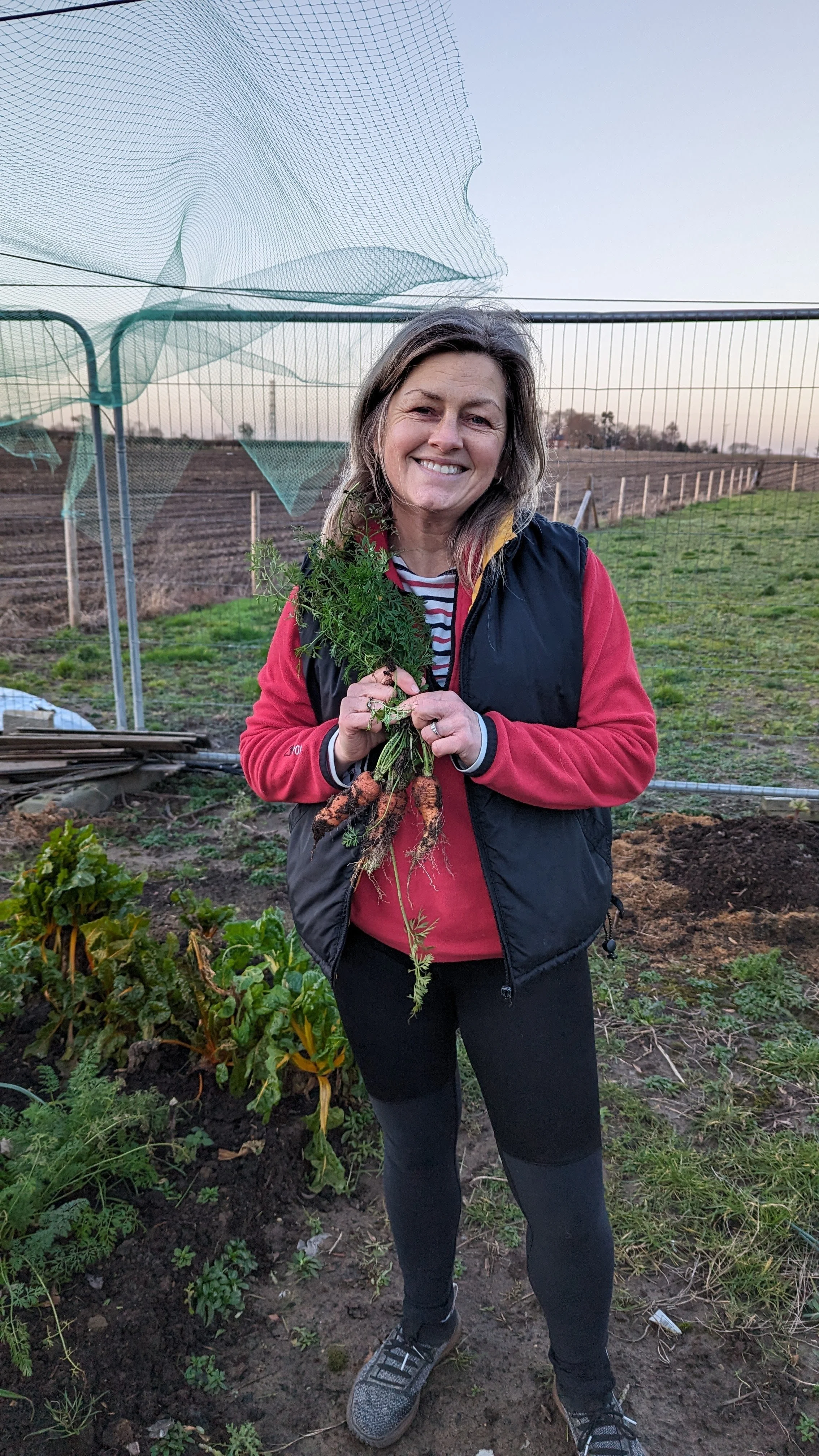 Happy smiling woman holding her own grown carrots out in Norfolk
