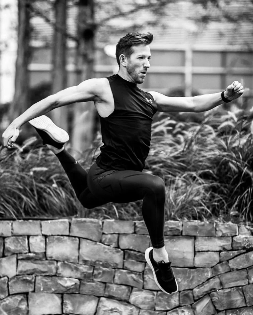 Man performing a parkour move jumping over a stone wall outdoors.