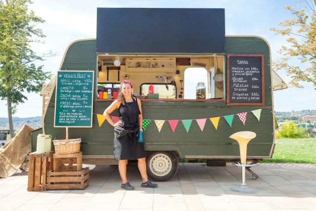  Photo:  One woman (food truck owner) standing in front of her food trailer.  