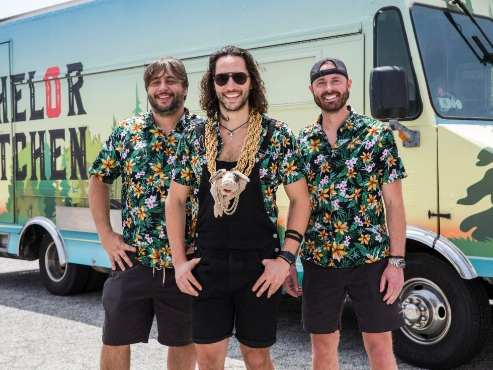  Photo:  Three men (food truck owners) standing in front of their food truck wearing matching Hawaiian shirts.  
