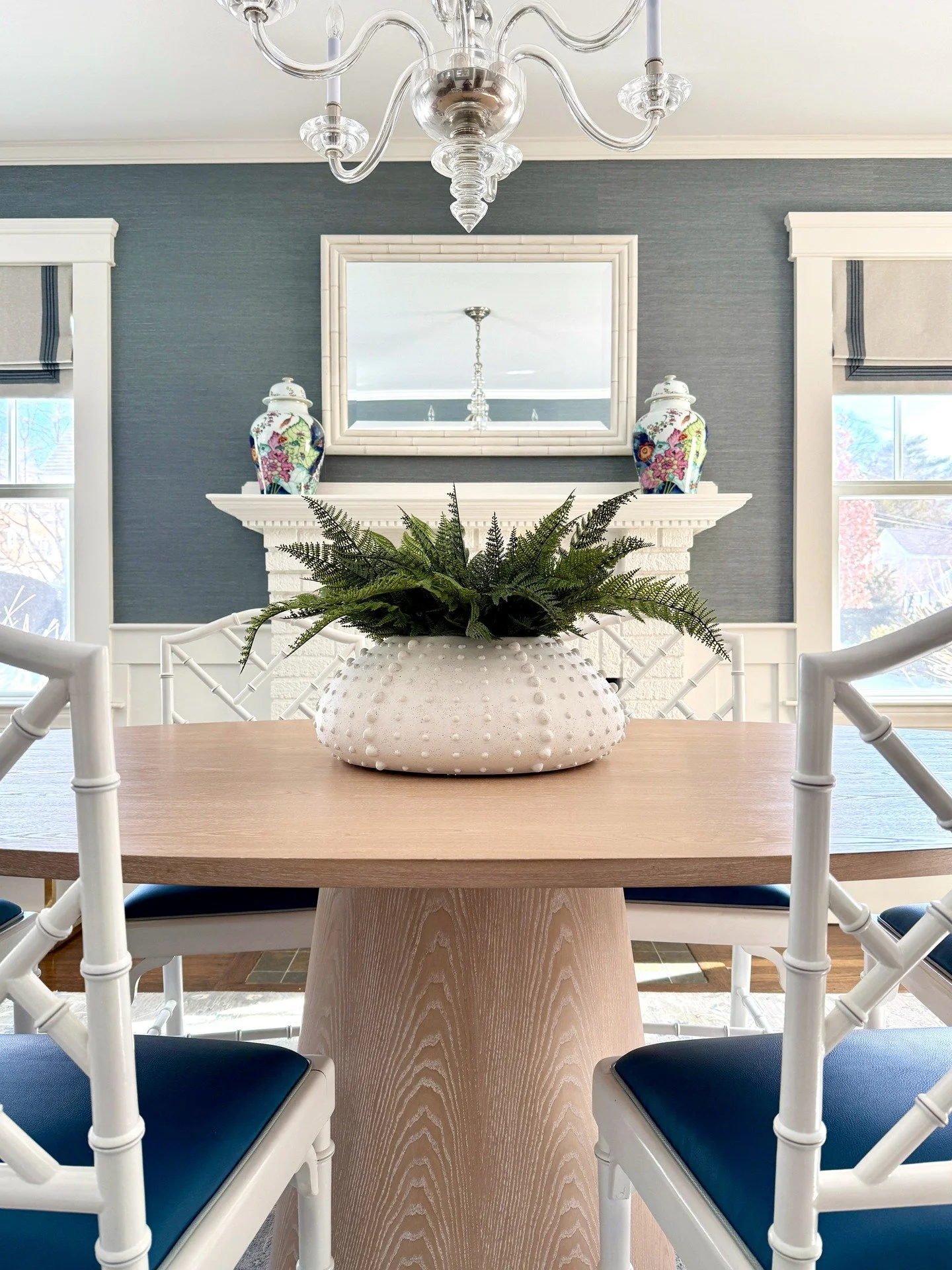 Sunlit, layered, and effortlessly timeless. This dining room blends classic architecture with fresh, tailored details&mdash;smokey blue grasscloth wallpaper, a statement chandelier, and blue and teal accents that include a peacock faux leather dining