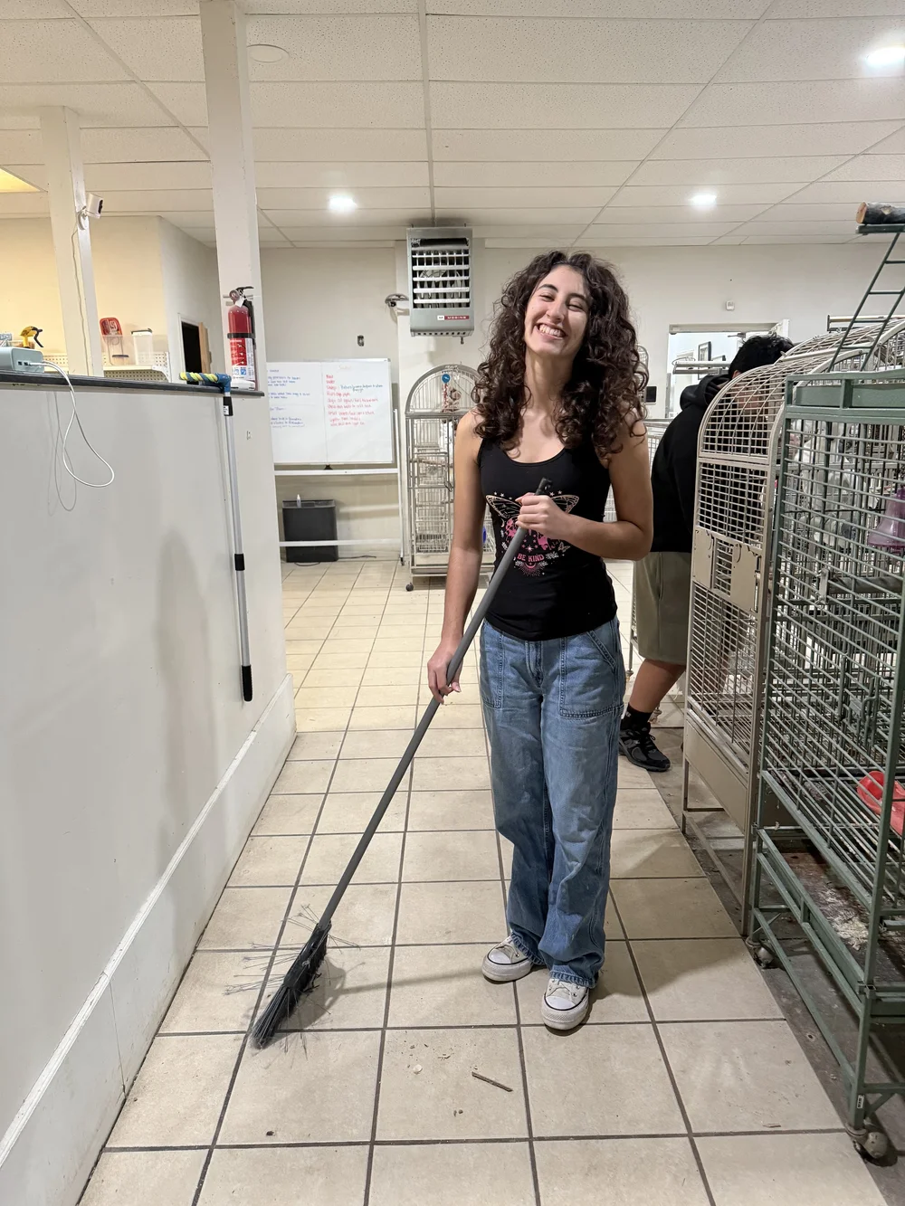 Smiling volunteer holding a broom in the bird-care room