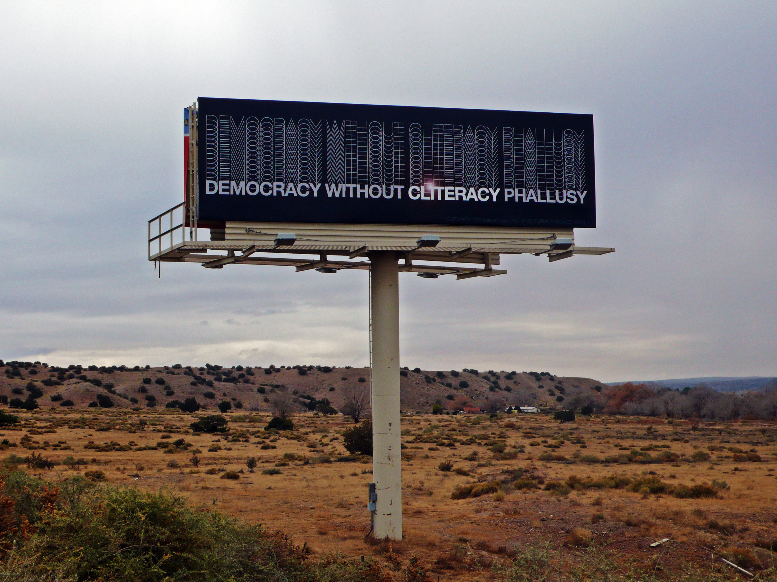   DEMOCRACY WITHOUT CLITERACY PHALLUSY,  Natural Law No. 57, 2013  Vinyl, Billboard 35 x 10.6 feet Exhibition on view November 11-25, 2013 on I-25 Southbound near mile marker 247.2. 