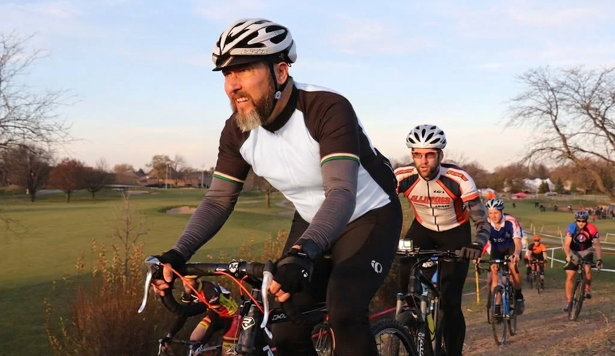 Group of people riding bikes on a paved trail in a park with grassy fields and leafless trees, under a clear sky.