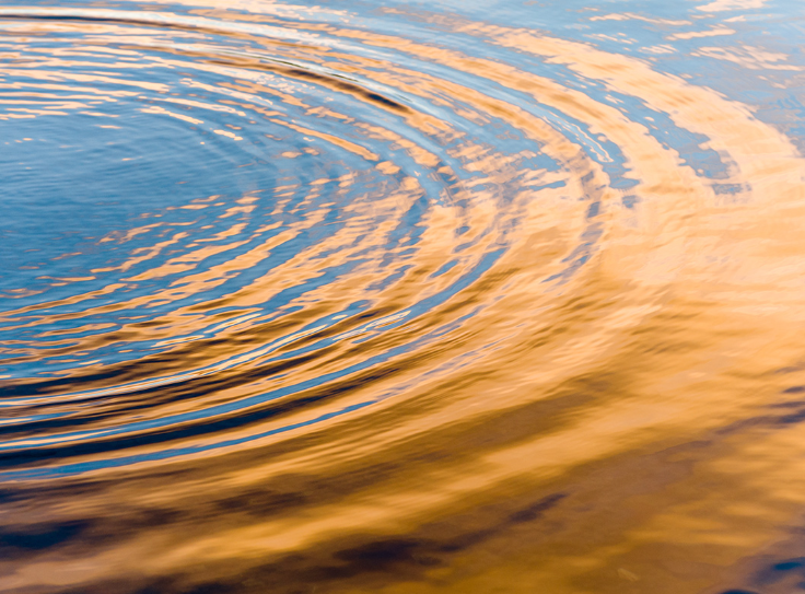 Close-up of rippling water reflecting the warm colors of a sunset.