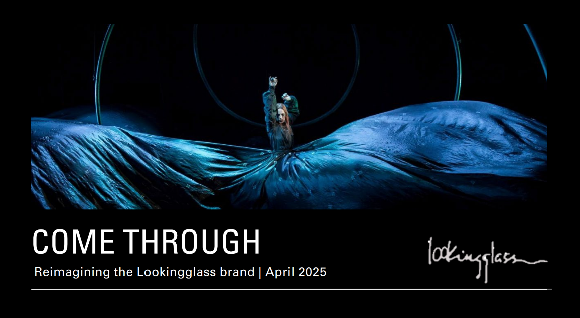 A woman on stage raising her right arm with her hand in a fist, wearing a long flowing black dress, performing under blue lighting with circular light fixtures in the background.