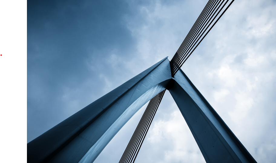 Looking up at the underside of a large, modern suspension bridge with cables extending from the towers to the roadway, set against a cloudy sky.