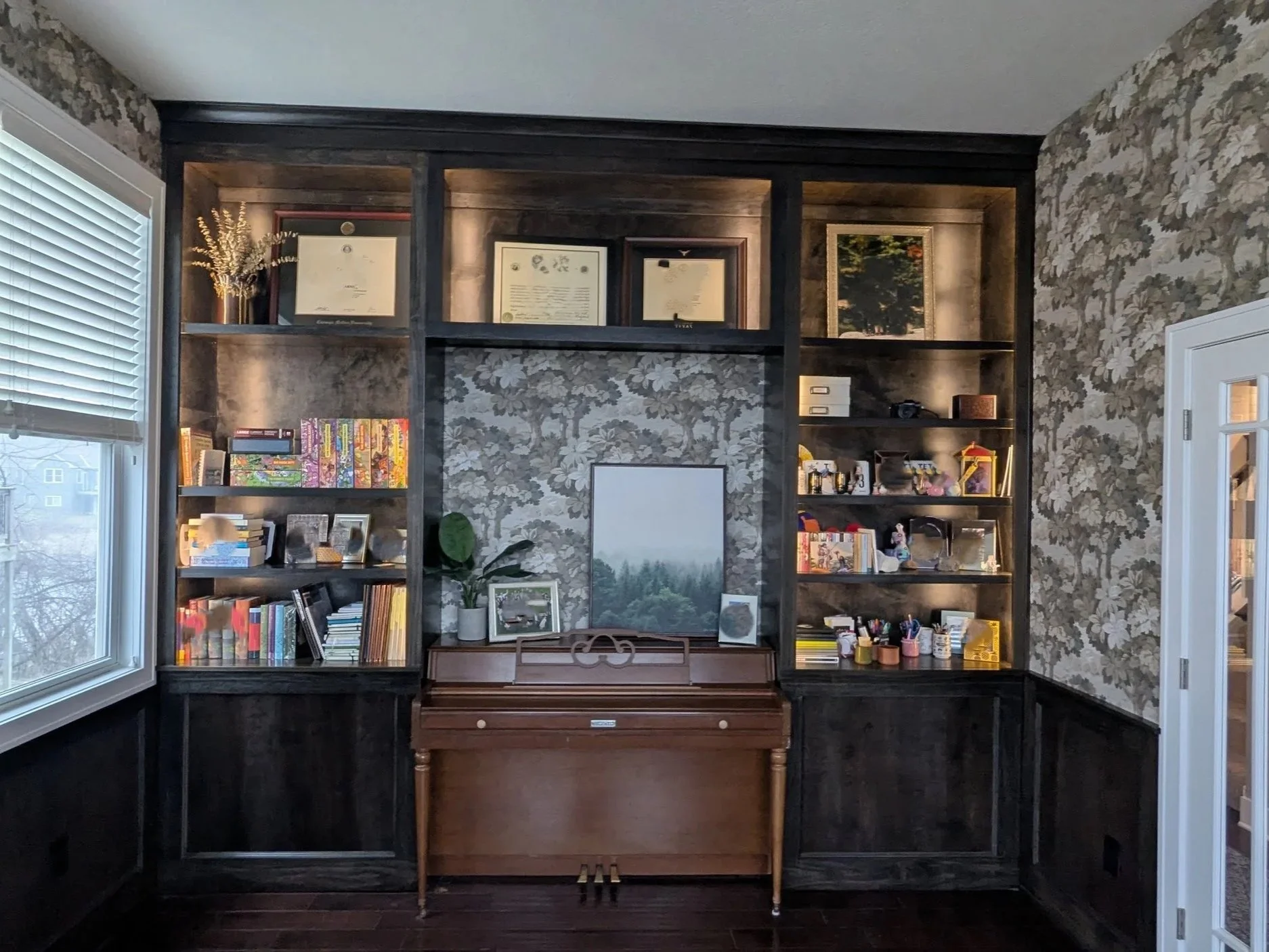 Custom lighted shelving installed around a piano with wall treatment 