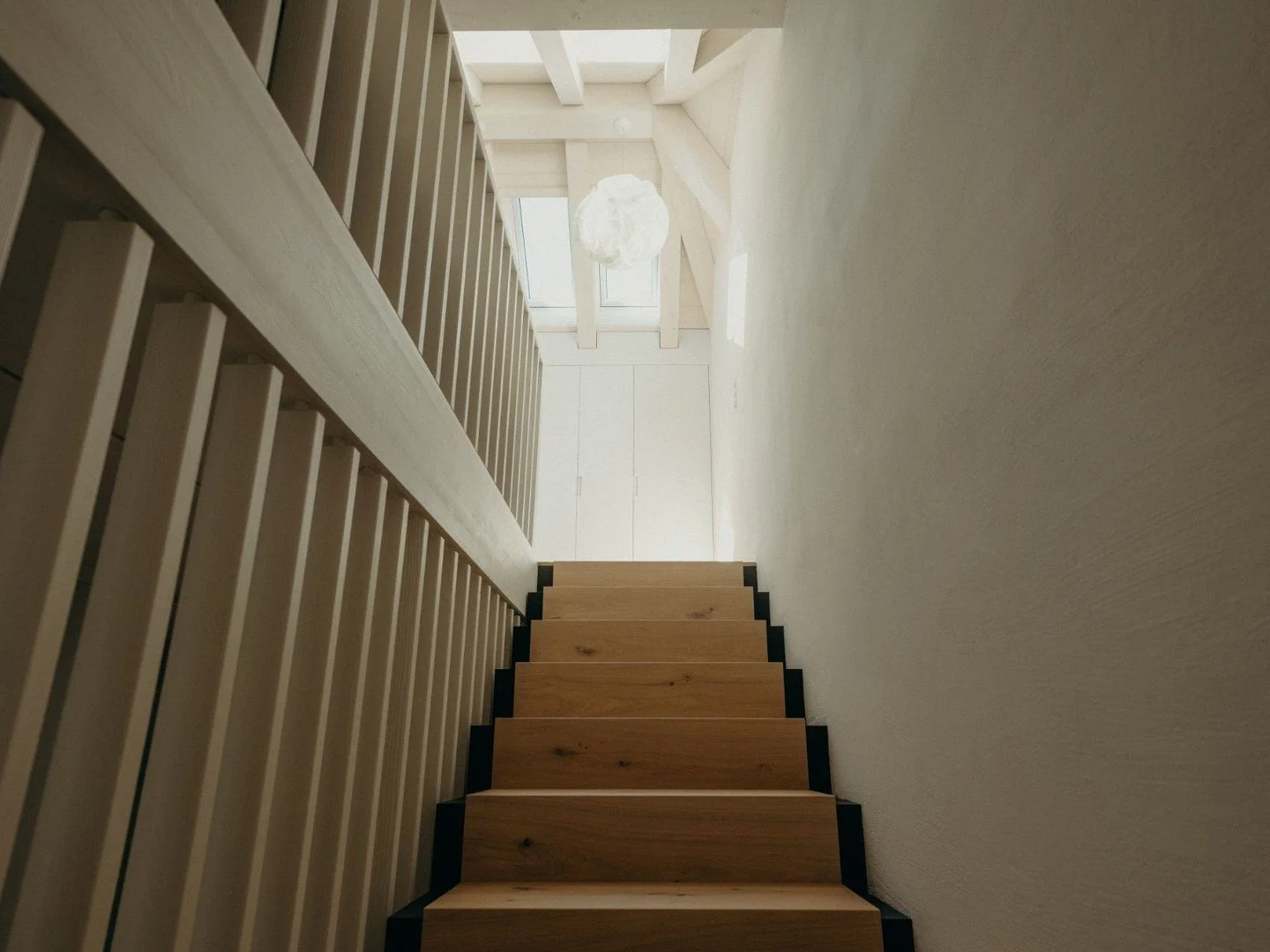 [Treppe mit Durchblick]
Die Holztreppe f&uuml;hrt ins Dachgeschoss, welches durch die Dachfenster in hellem Licht erstrahlt. Die Materialisierung vom Holz wird auch beim Fallschutz von Dachgeschoss bis Erdgeschoss durchgezogen und verbindet die Ebene