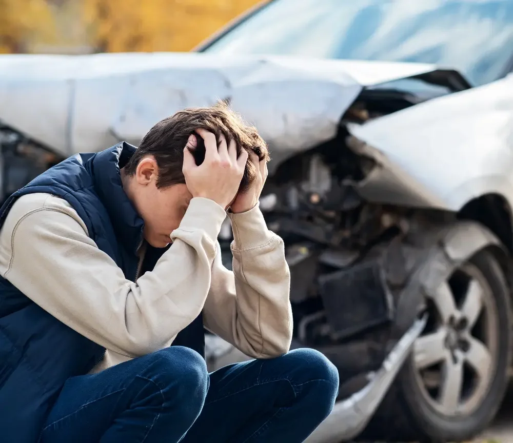 Frustrated man sitting outside broken vehicle in need of Classen-Ten-Penn OKC car accident doctor