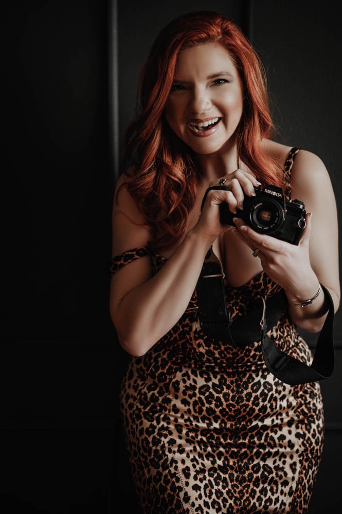 Smiling woman in leopard print dress holding a camera.