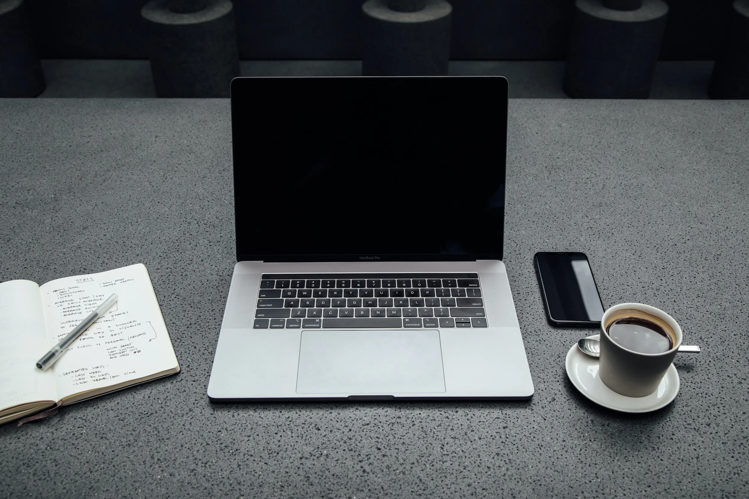 Open laptop on desk with notebook, pen, smartphone, and coffee cup.