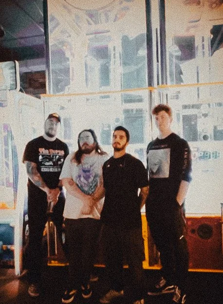 Four people standing together inside a gaming arcade, with vintage arcade game machines visible in the background.