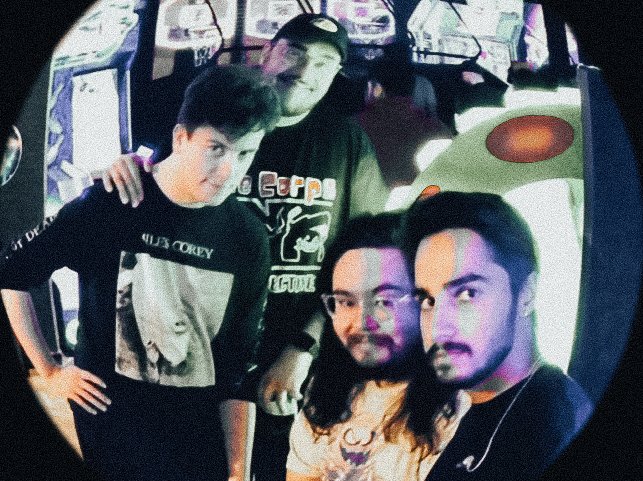 Group of four young people taking a selfie inside an arcade with a racing game in the background.