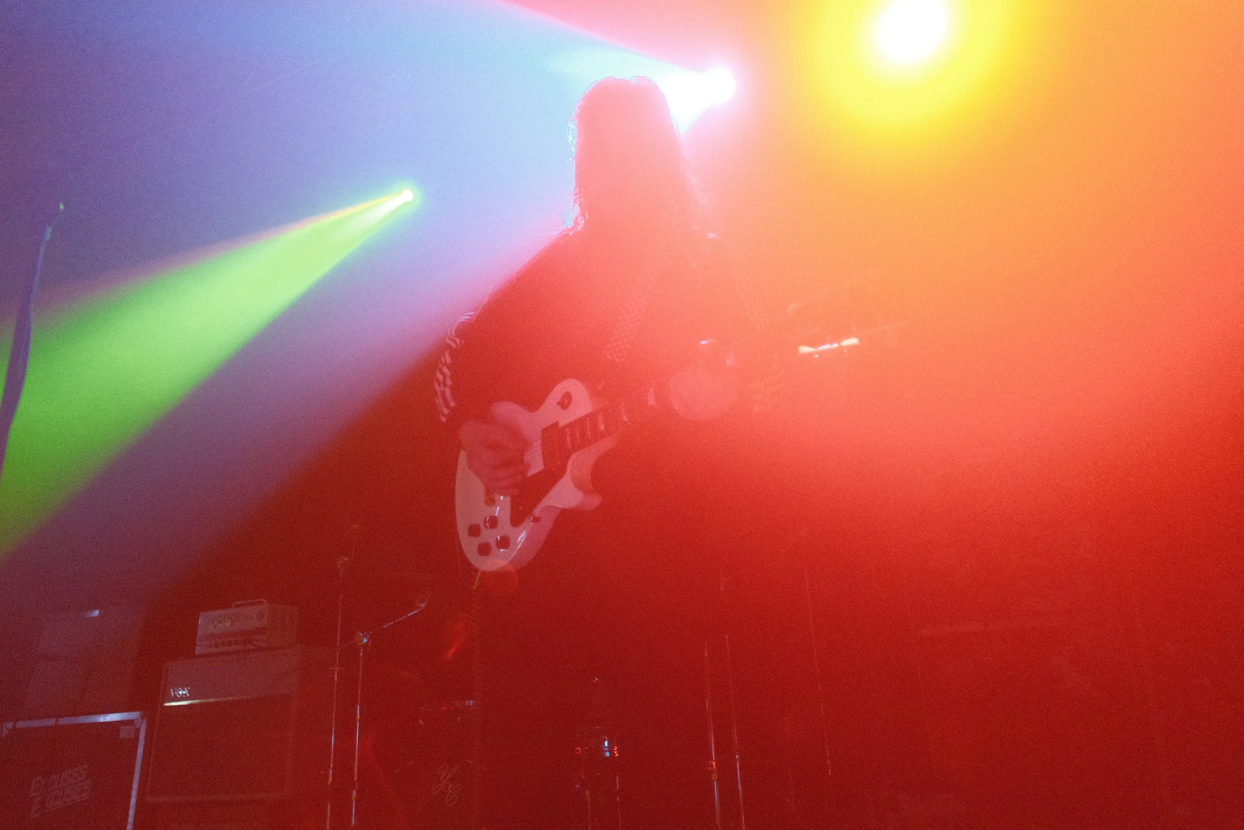 A person playing a guitar on stage with colorful stage lights creating an atmospheric glow.