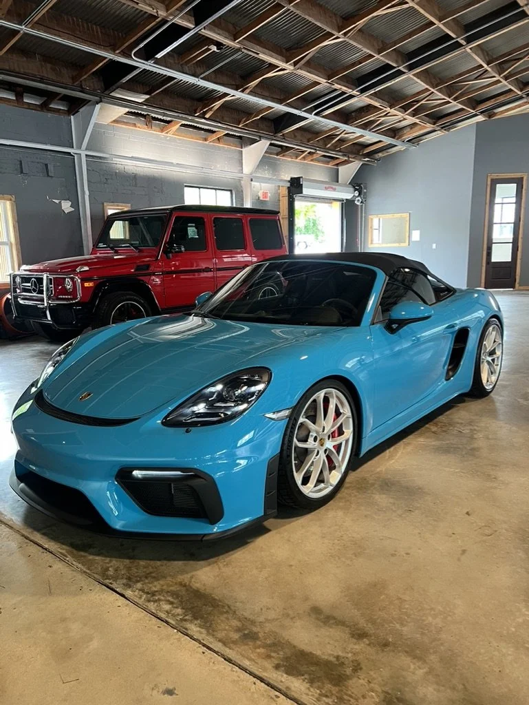 Blue Porsche sports car showcasing a ceramic coating parked inside a garage with a red Mercedes-Benz G-Class vehicle in the background.
