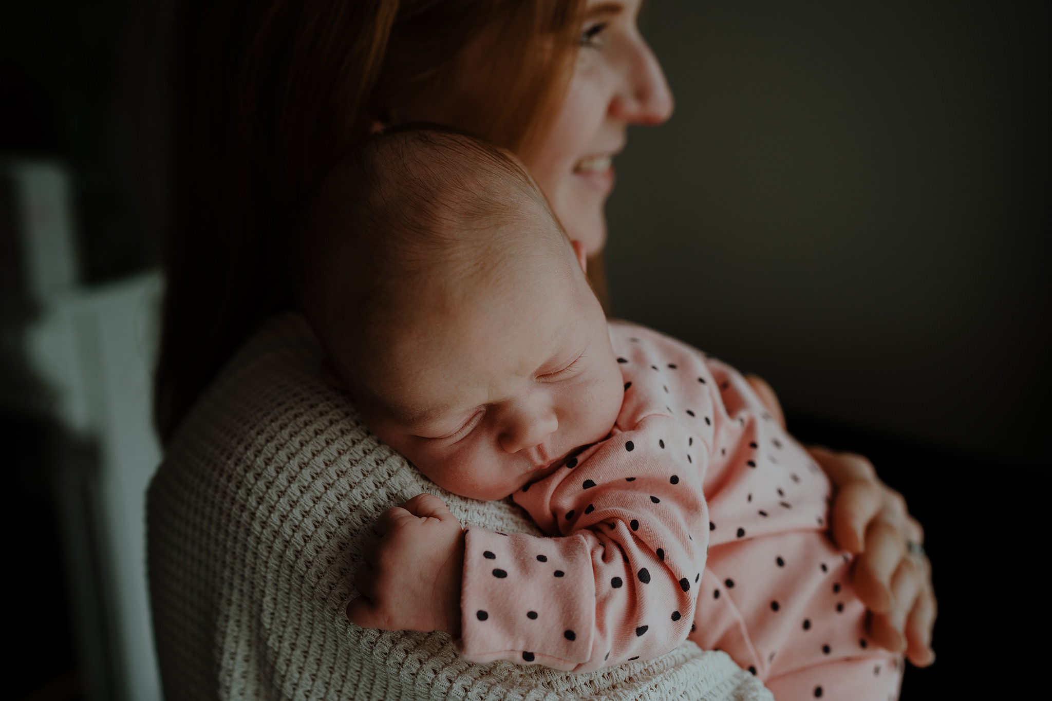 A woman holding a sleeping baby, close-up of their faces and upper bodies.