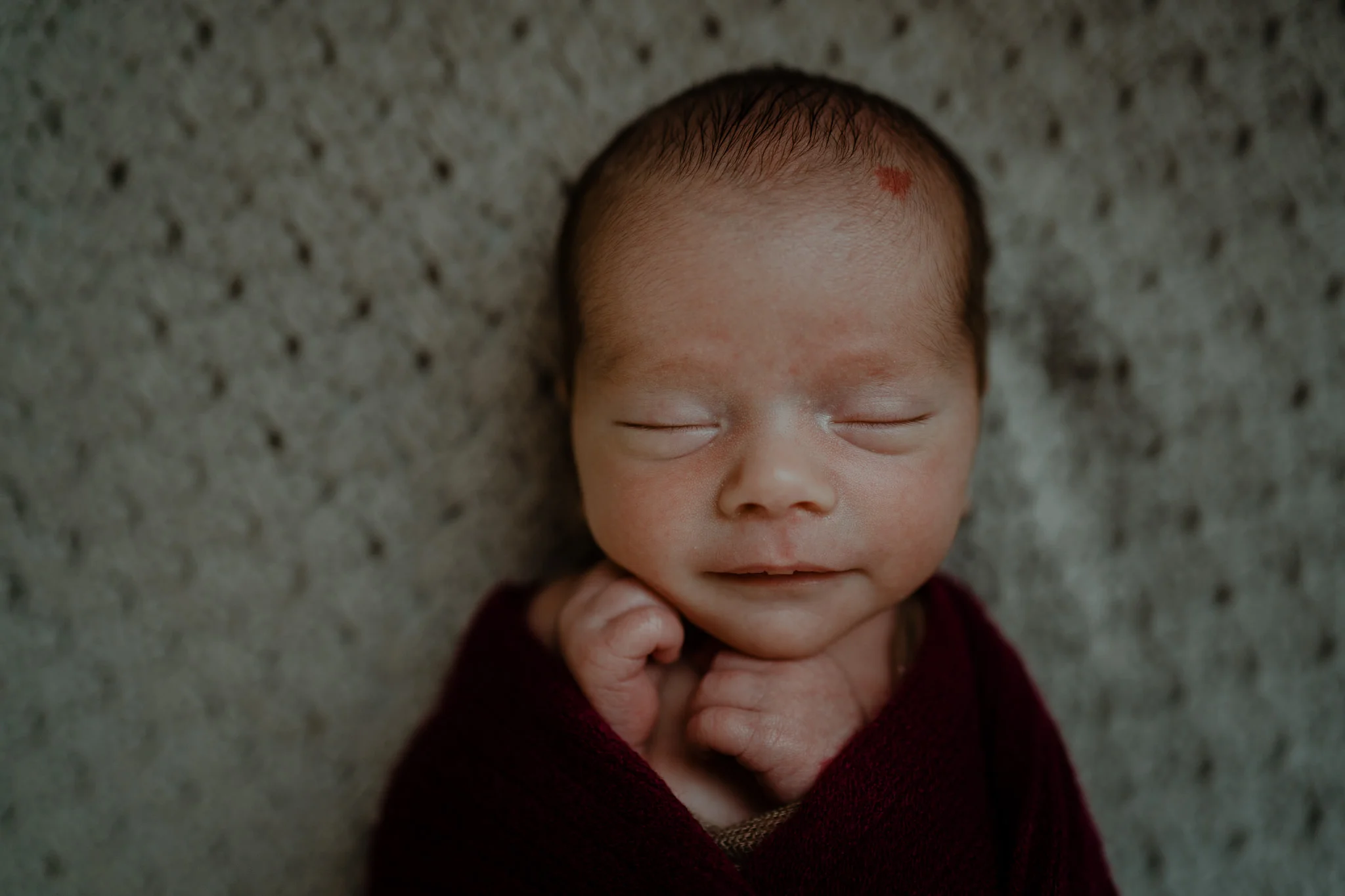 Newborn baby boy in burgundy wrap