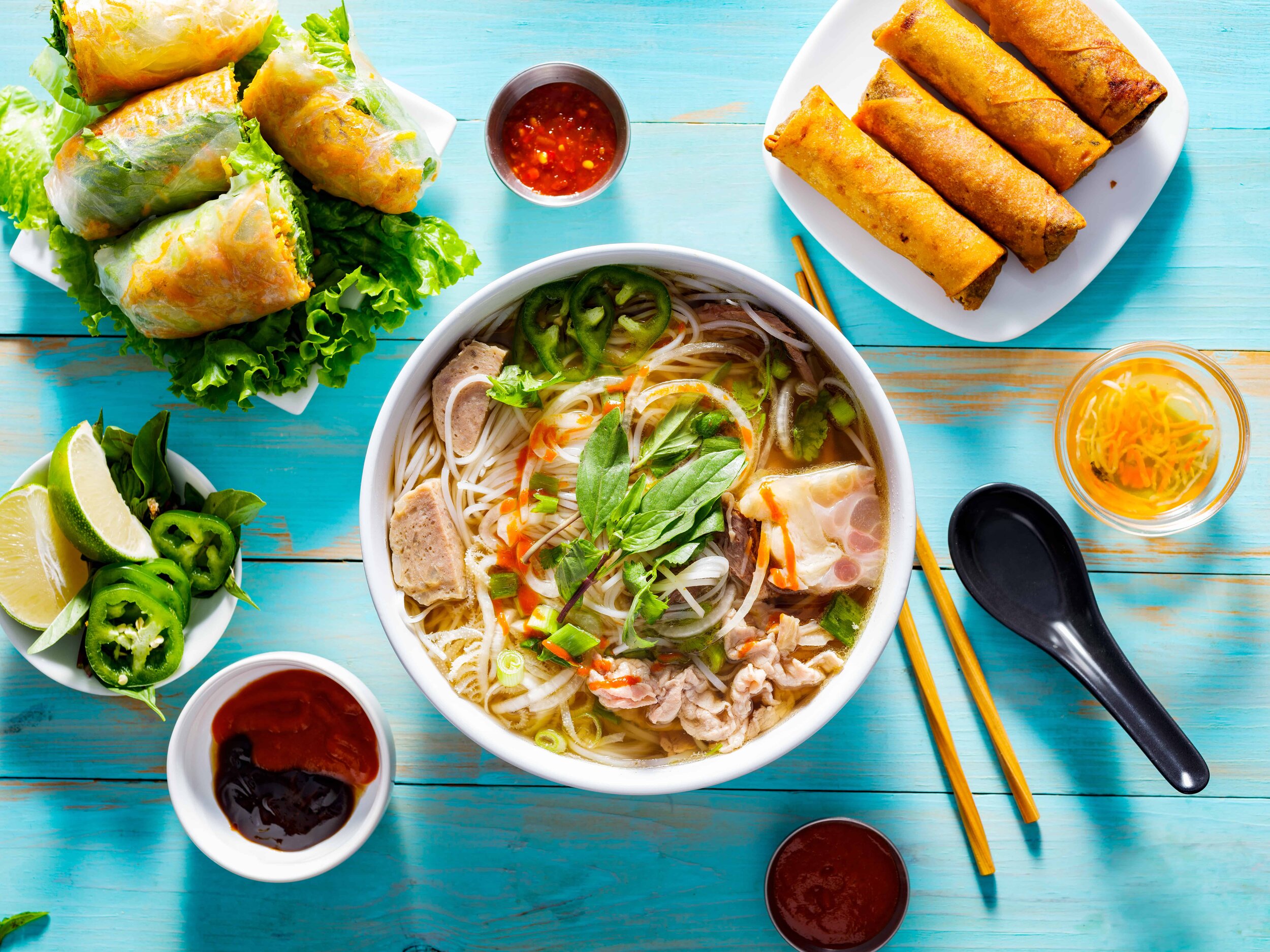Canva - Vietnamese Pho Bo Soup with Appetizers on Table and Drizzled with Sriracha Sauce (1).jpg