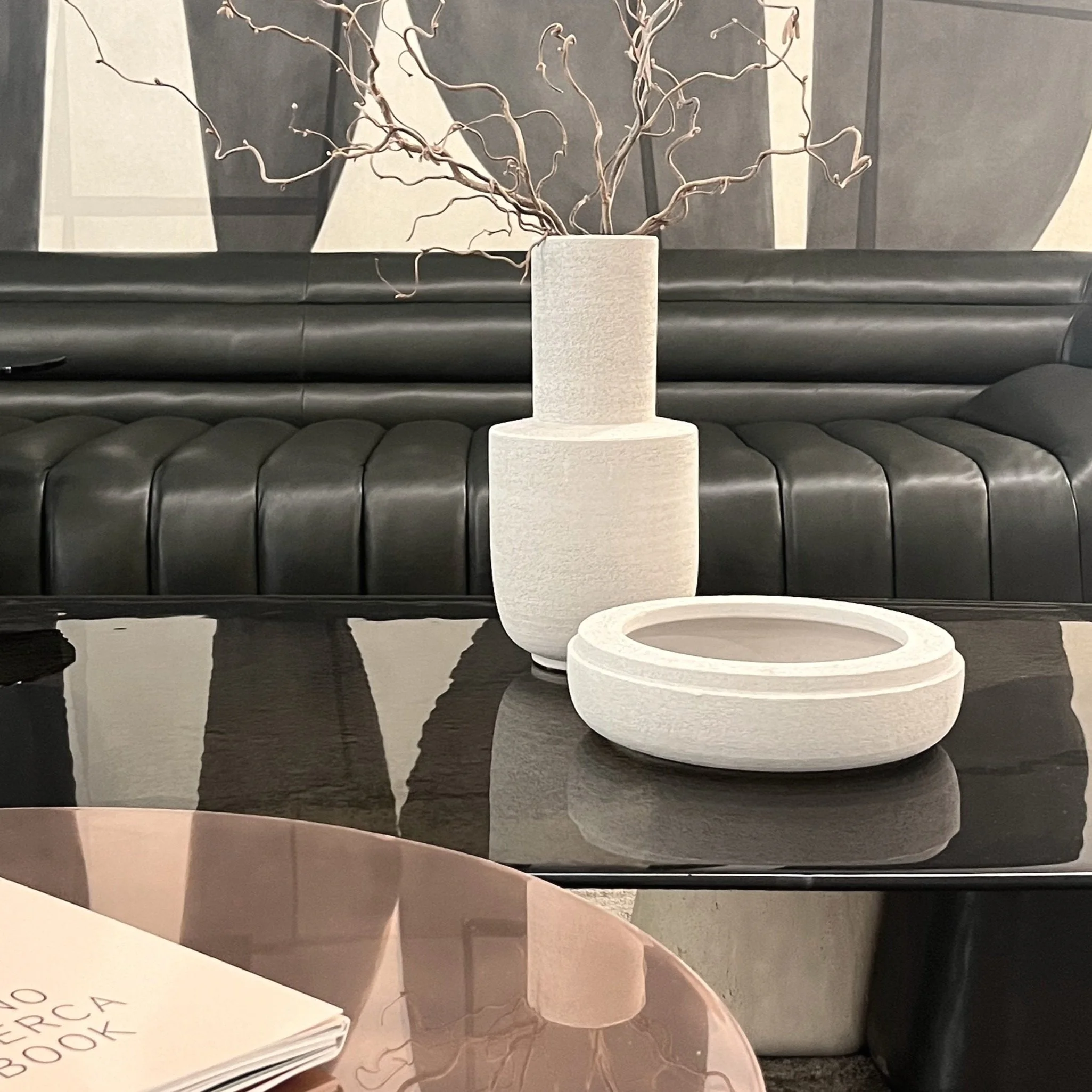 Decorative vases with branches on a black stove, placed on a black coffee table with a pinkish round table in the foreground.