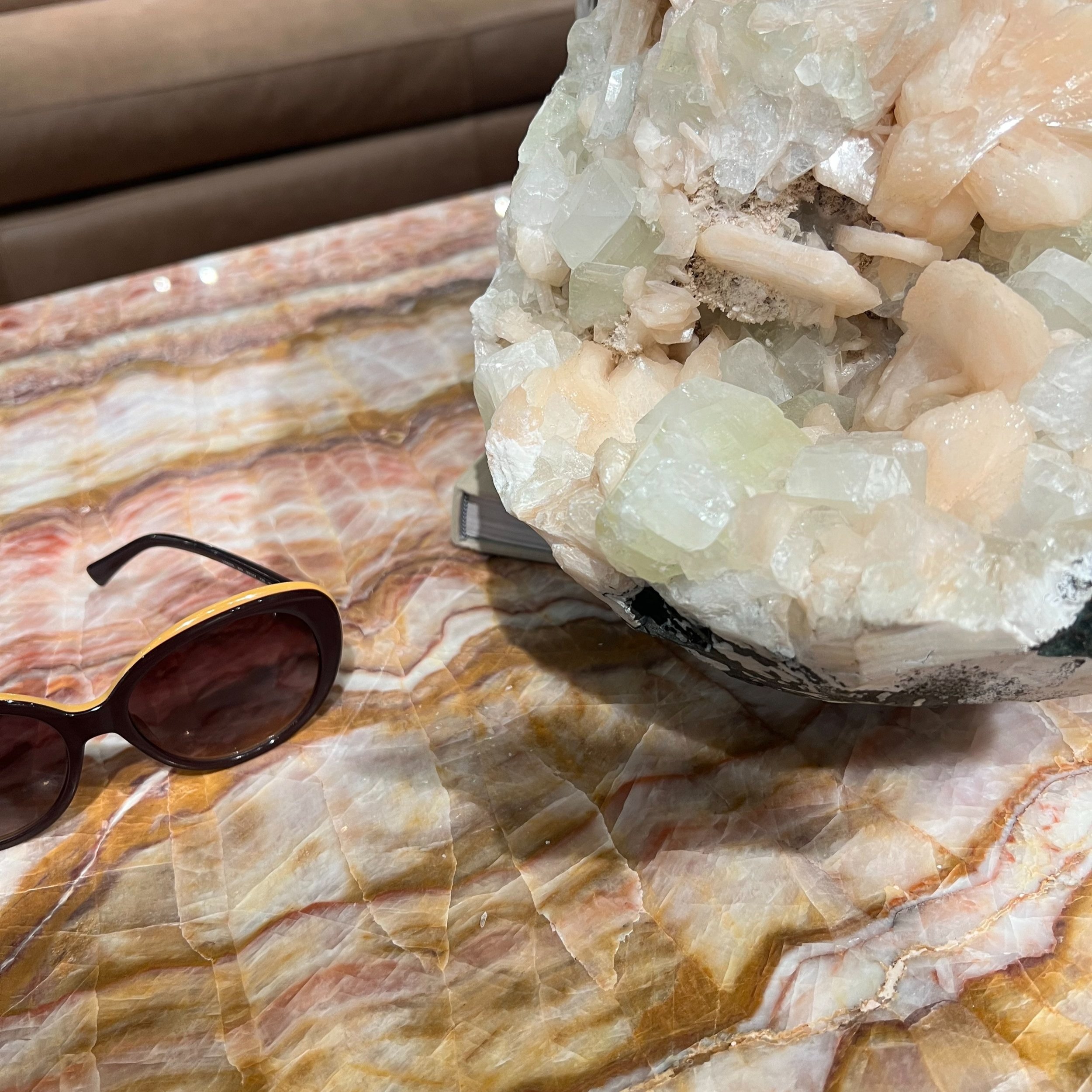 A large mineral or crystal rock, a pair of sunglasses with dark lenses, and a small notebook on a polished, multicolored marble surface.