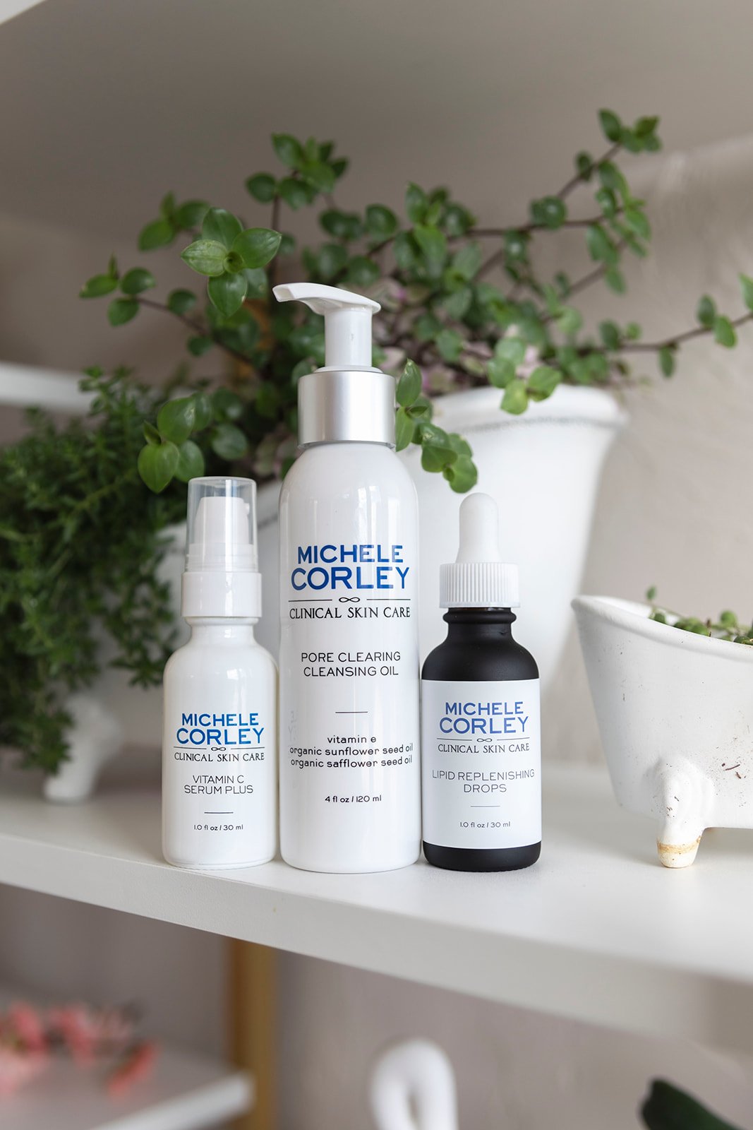 Skincare products on a white shelf with potted plants in the background.