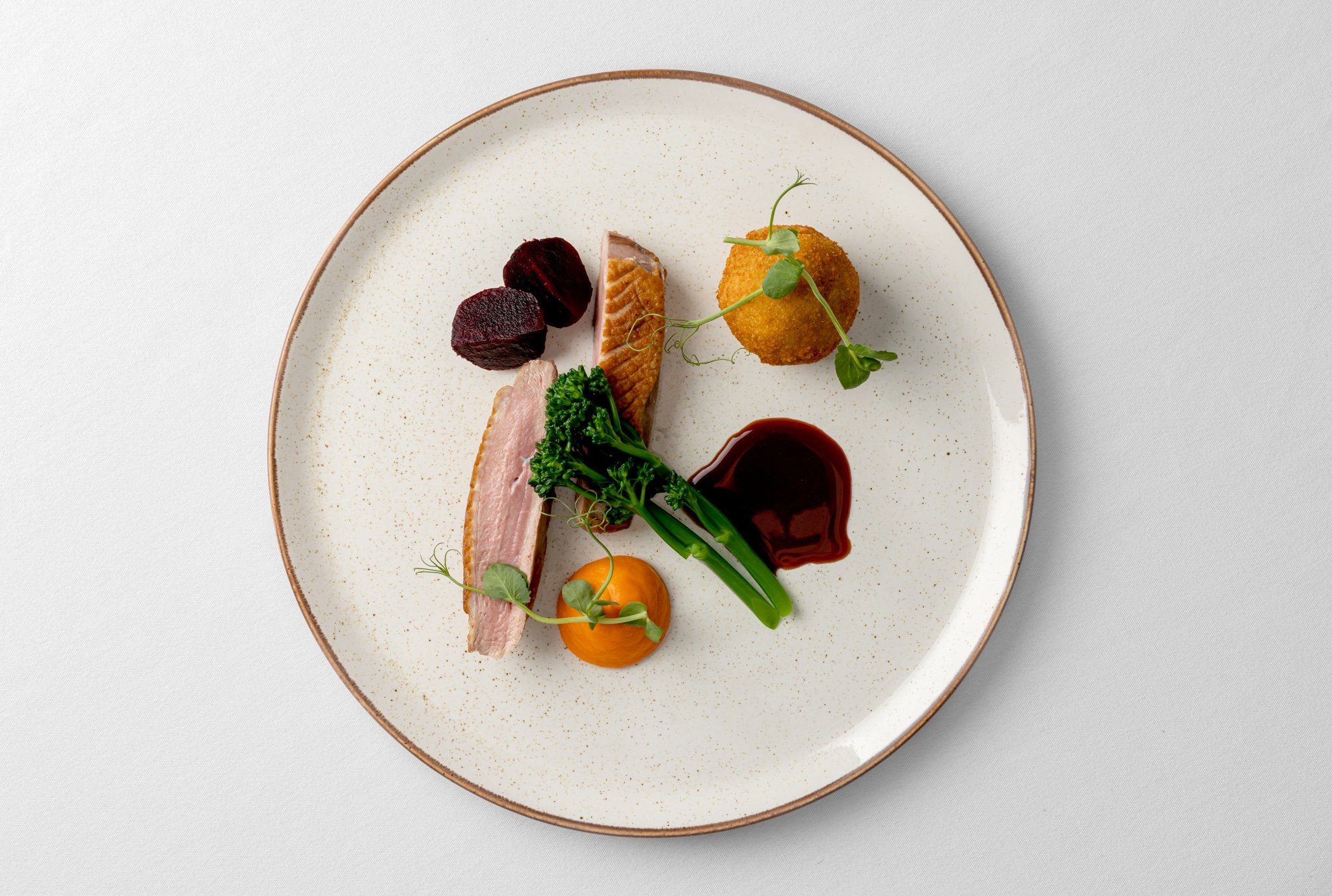 Duck, tenderstem broccoli, spiced carrot puree on natural plate