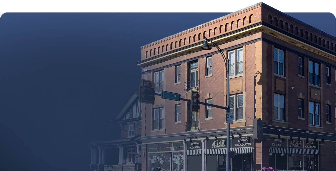 A four-story brick building on a street corner with an ice cream shop on the ground floor, street signs, and traffic lights. The building has multiple windows and decorative brickwork at the top.