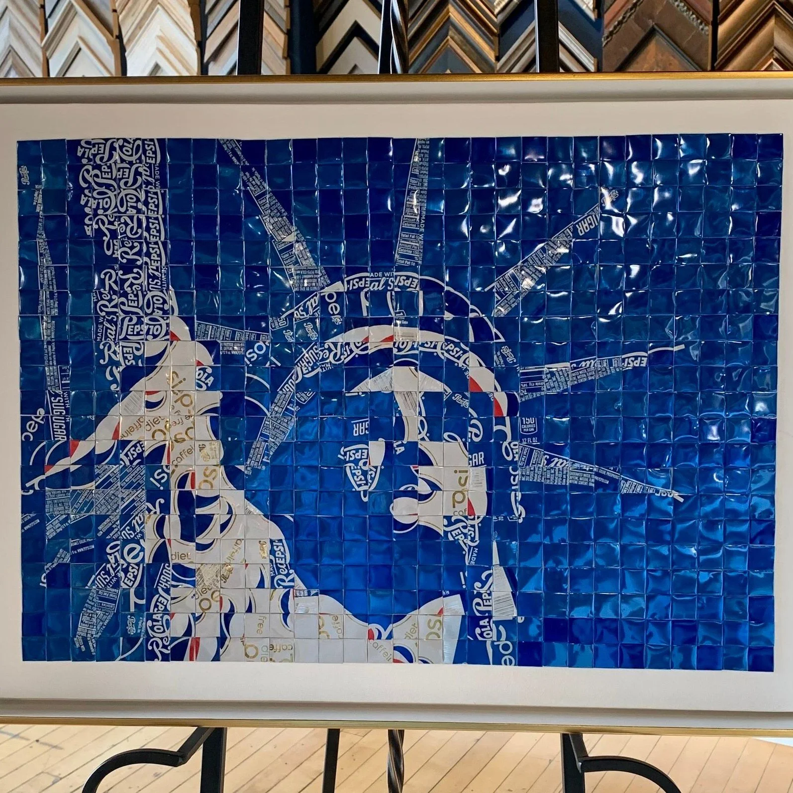 This awesome piece is so unique! This Statue of Liberty is composed entirely of folded Pepsi Cans! We are so impressed by the talent and patience this took! Together we chose a white and gold frame to really bring out the gold details of the cans and