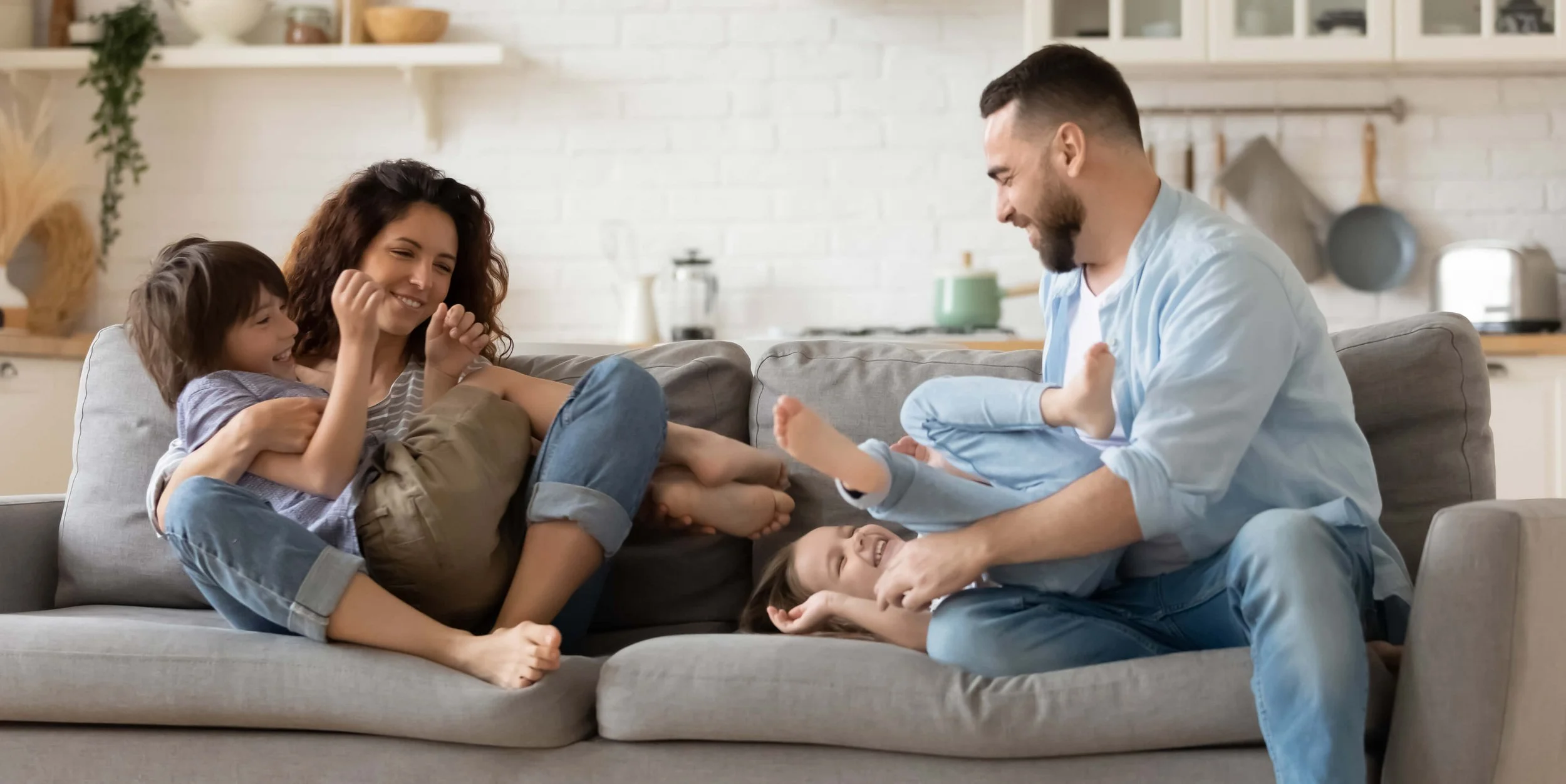 A picture of a family of four playing on a living room couch. The family has no worries because their house has working a great water heater..