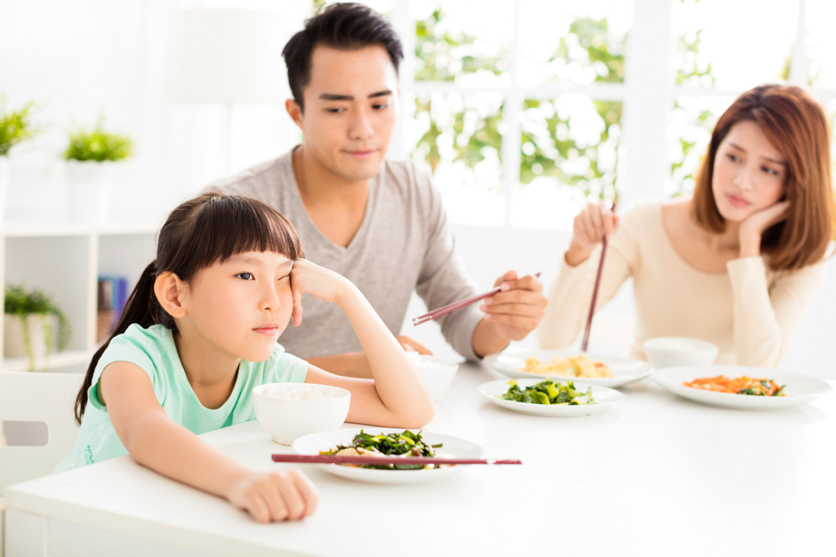 young girl refusing to eat at dinner table with parents