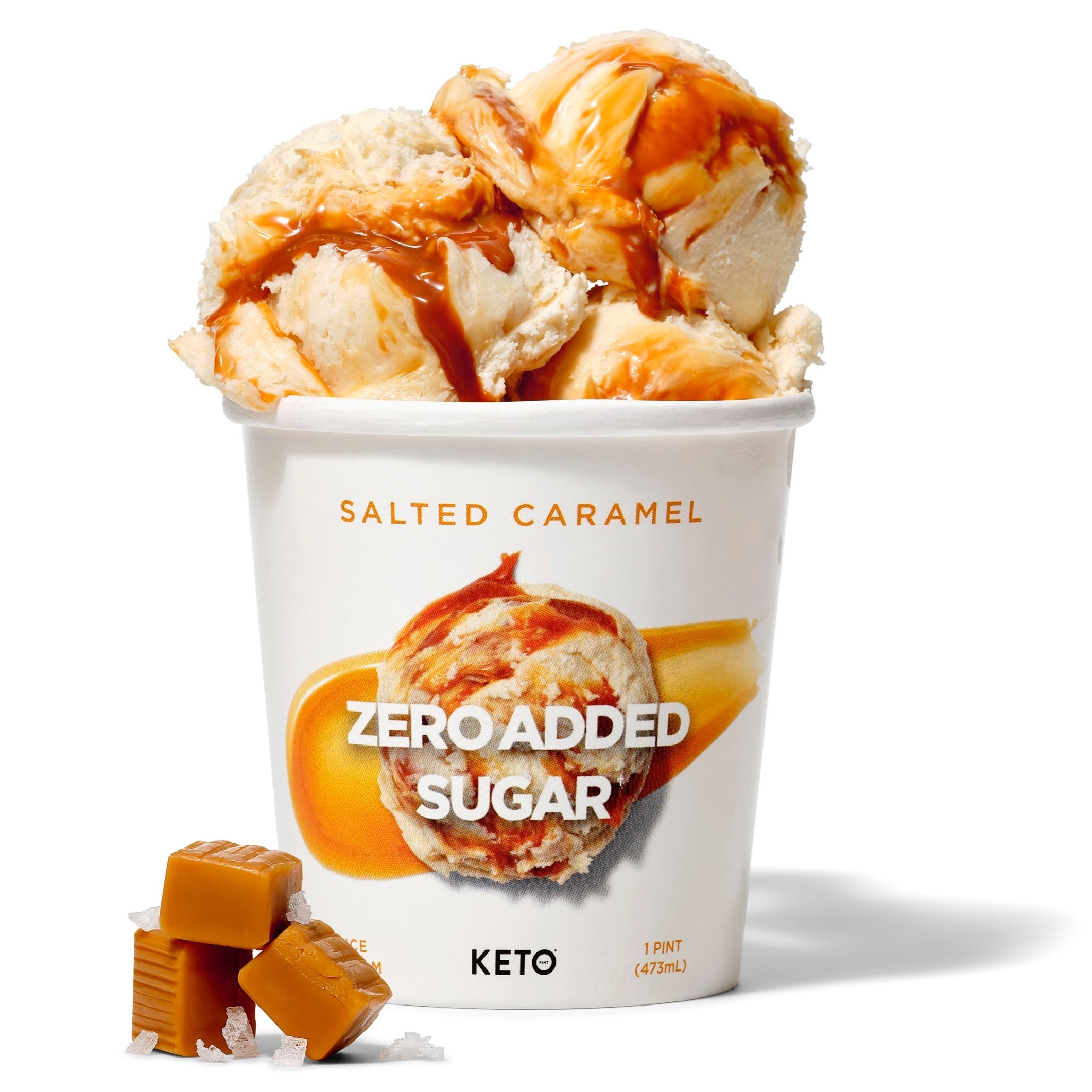 A cup of salted caramel ice cream with caramel drizzle on top, with two caramel candies and salt crystals beside it.