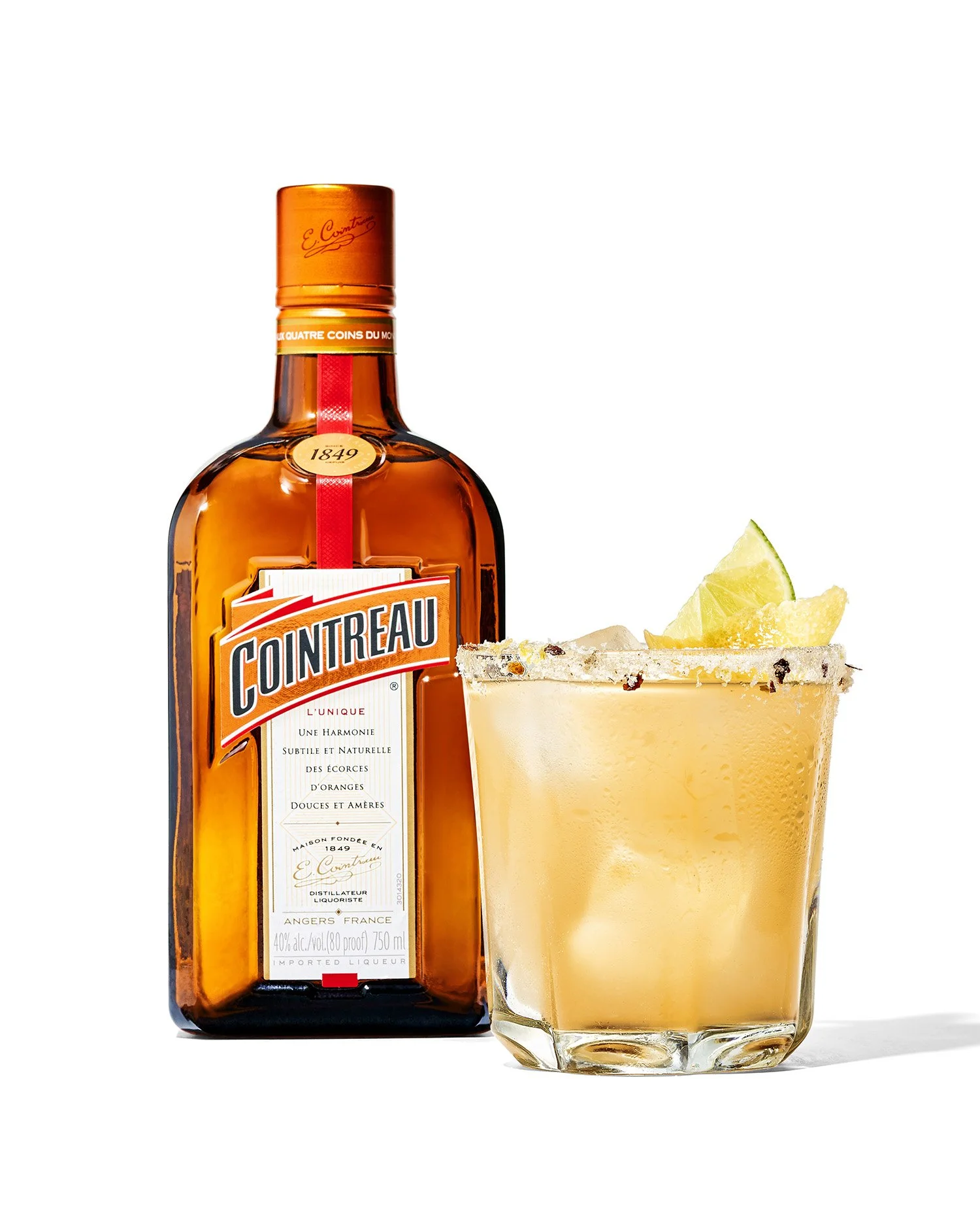 A bottle of Cointreau orange liqueur next to a cocktail glass with a salted rim, a lemon wedge, and a yellowish drink inside.