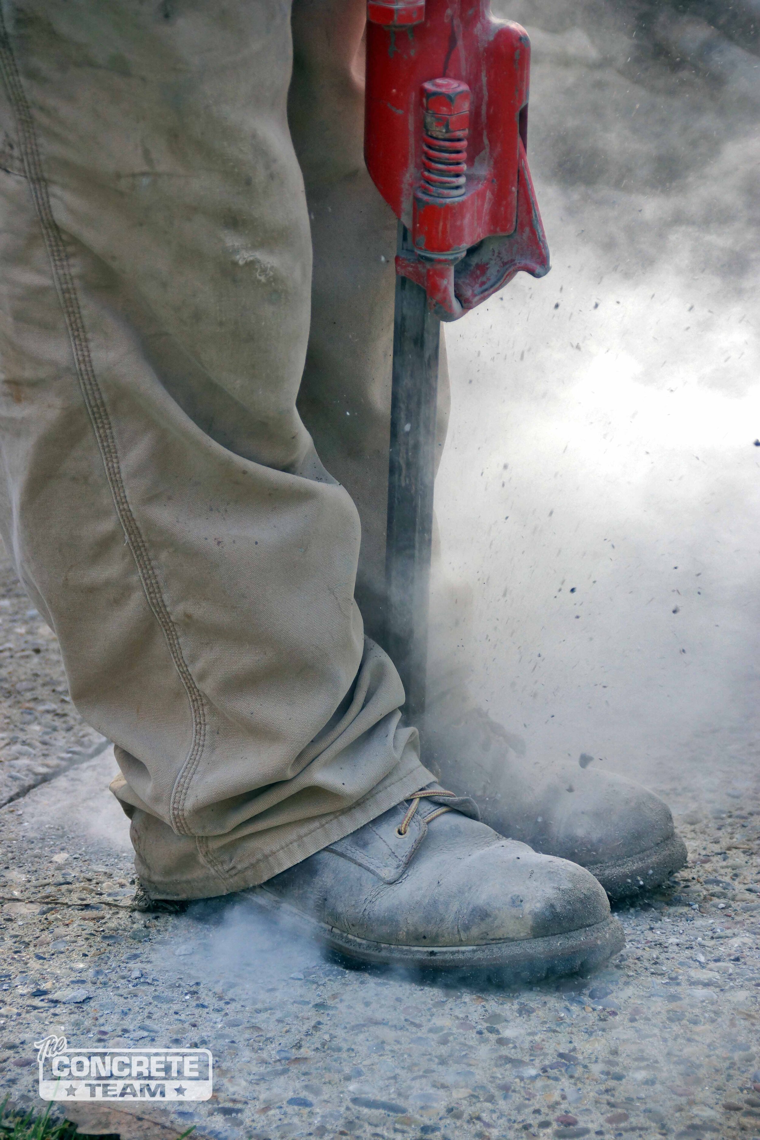  A close of image of a member of The Concrete Team drilling through a concrete slab in order mudjack or level the the slab to remove tripping hazards. 