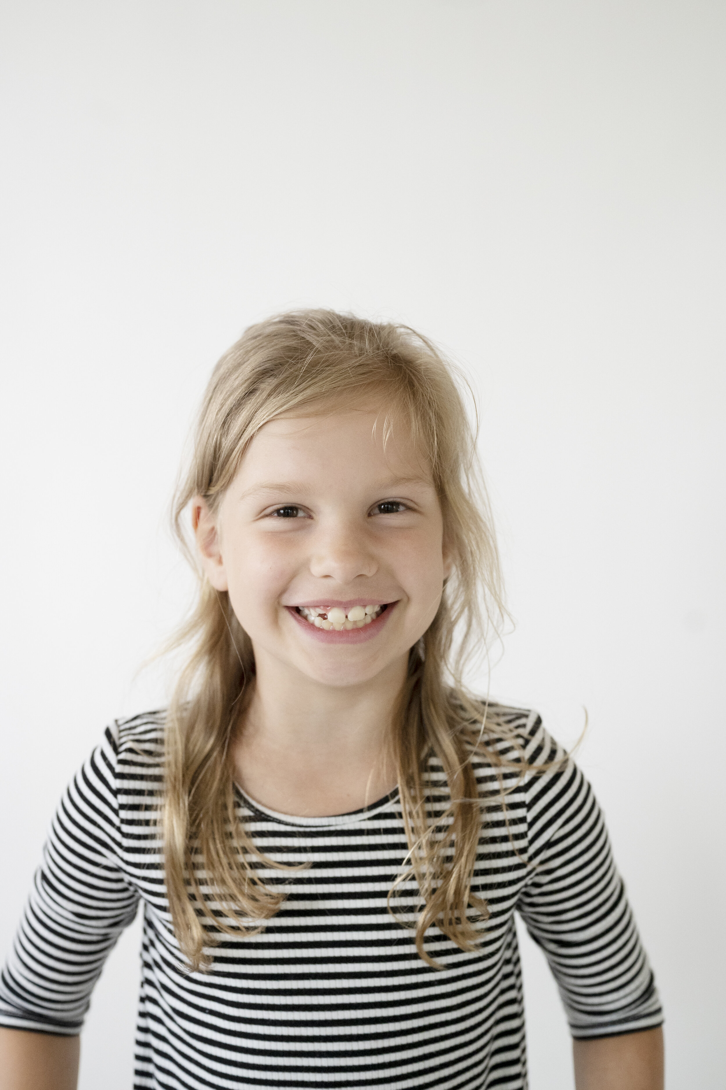 Young girl with reddish brown hair and a striped shirt is smiling directly at the camera.