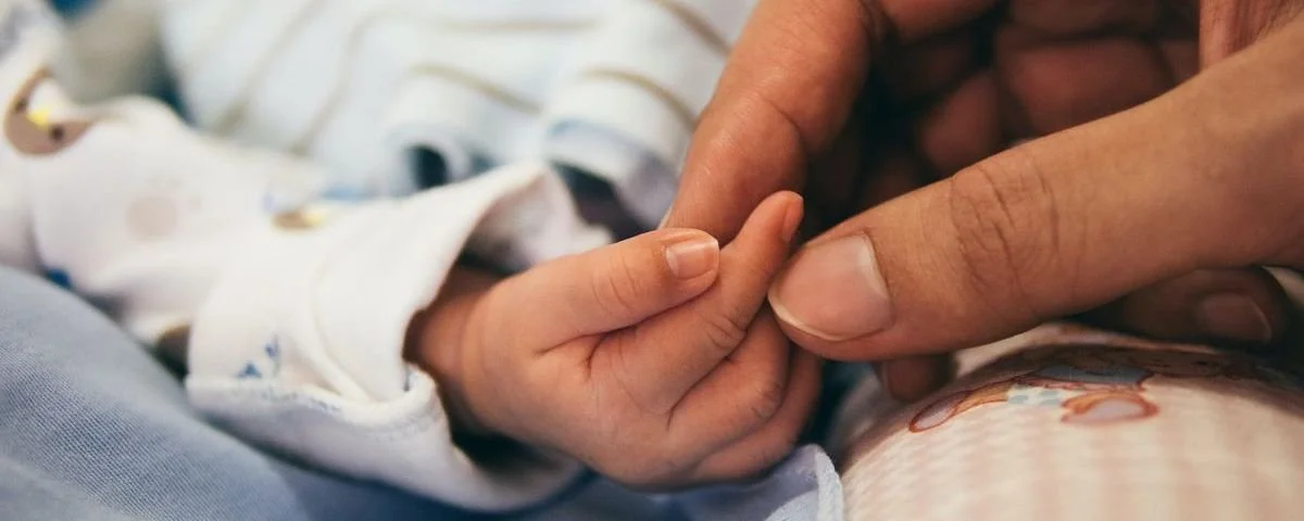 A close-up of an adult's finger holding a baby's tiny finger.