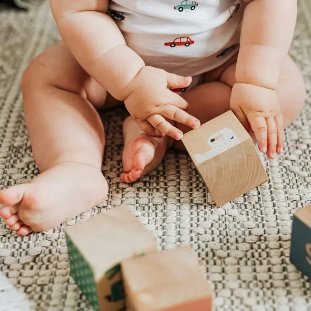 Baby sitting on a textured rug, holding a wooden block with a polar bear face, surrounded by other colorful wooden blocks.