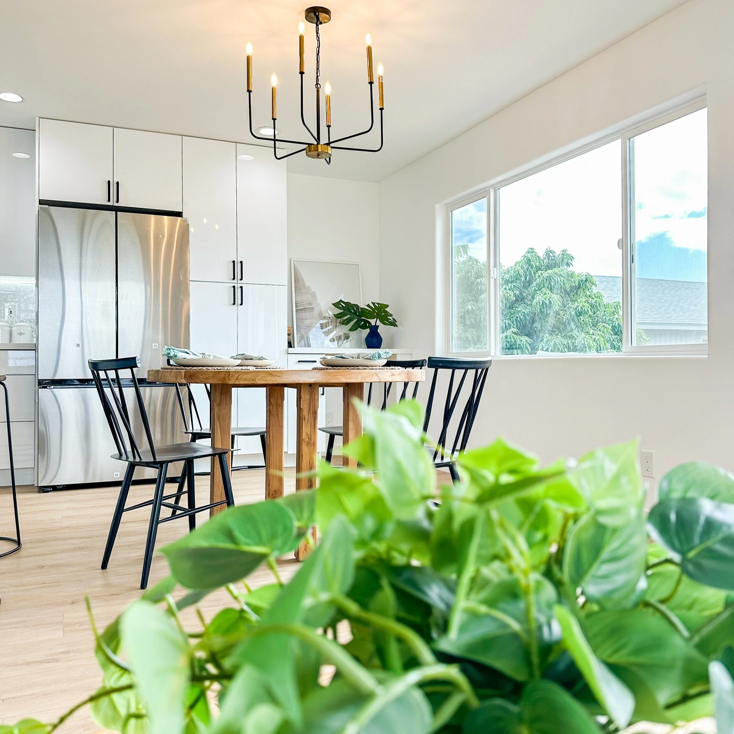 Bright kitchen and dining area staged by OASIS STAGING + DESIGN with a round wood table, black spindle chairs, and modern greenery