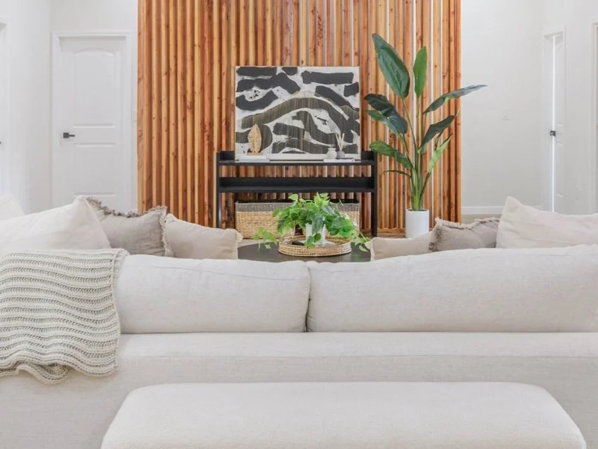 Neutral living room with soft-toned sectional, abstract art, and vertical wood panel backdrop styled by OASIS STAGING + DESIGN