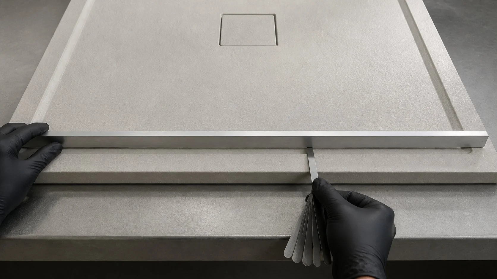 Technician checking a shower tray perimeter landing with a metal straightedge and feeler gauge