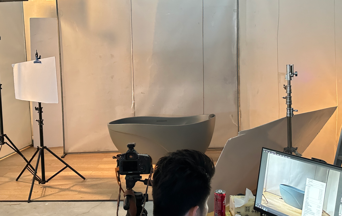 Photography studio setup with a modern freestanding bathtub, lighting equipment, and a person working on a computer.