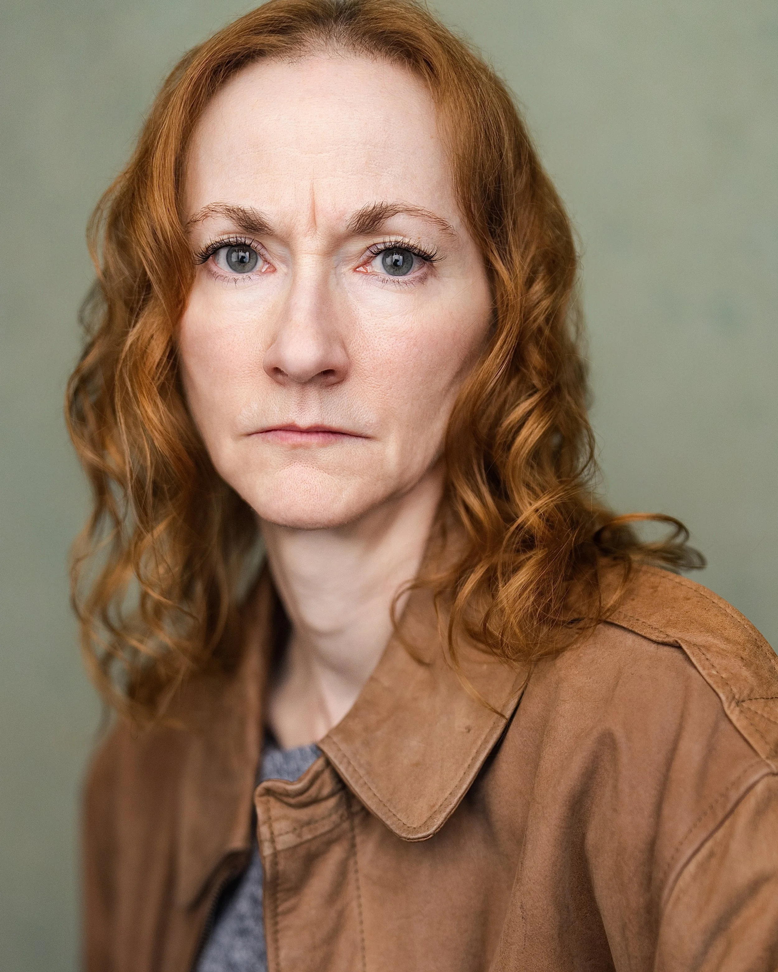 Redheaded woman wearing a brown leather jacket over a blue-grey jumper