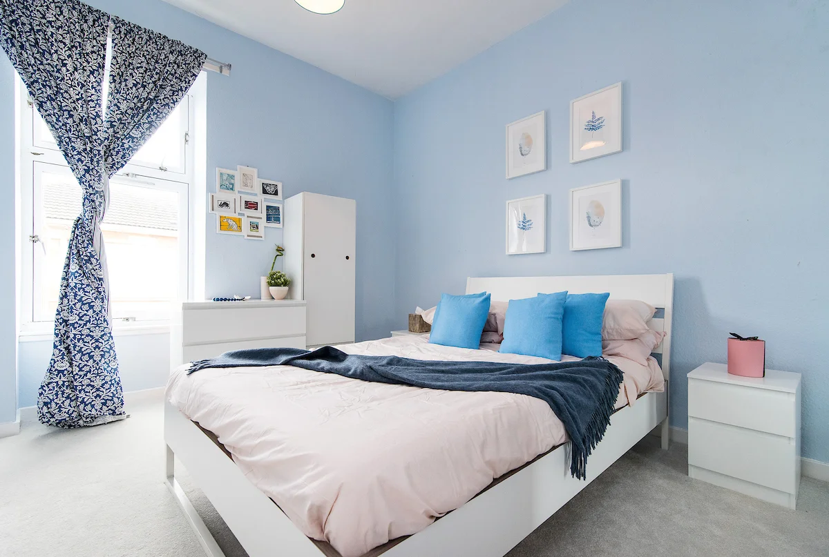 home staging, bedroom, blue walls, sunlight, white furniture, pink candles, frames