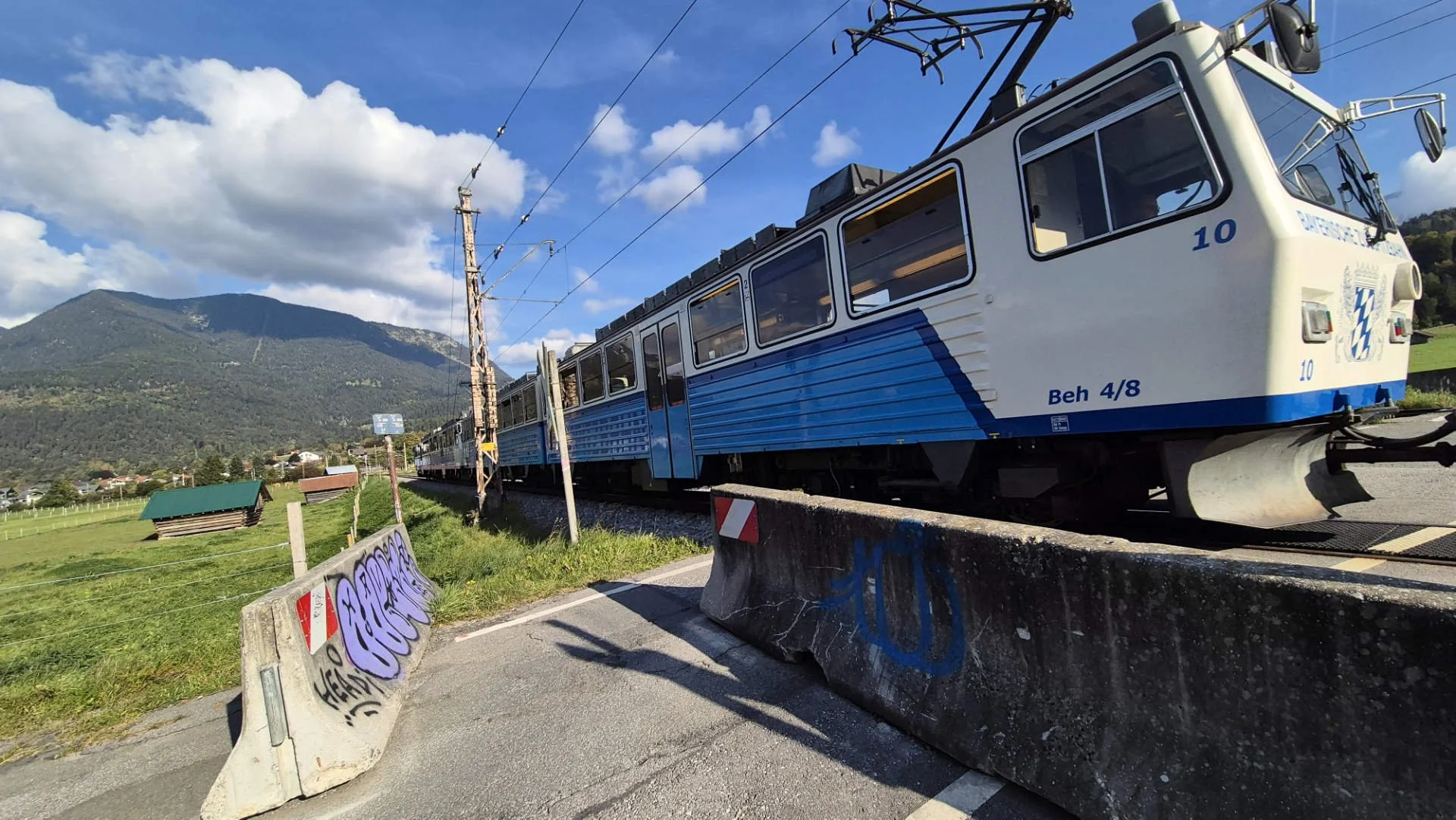 Zugspitzbahn mit blau-weißen Waggons beim Bahnübergang kurz vor der Station Garmisch-Hausberg