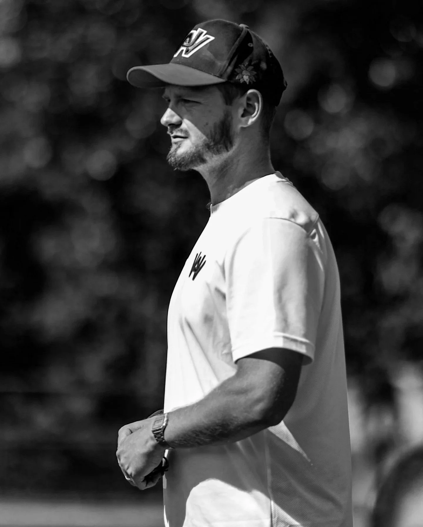 A soccer coach with a cap and sports jersey standing outdoors in black and white.