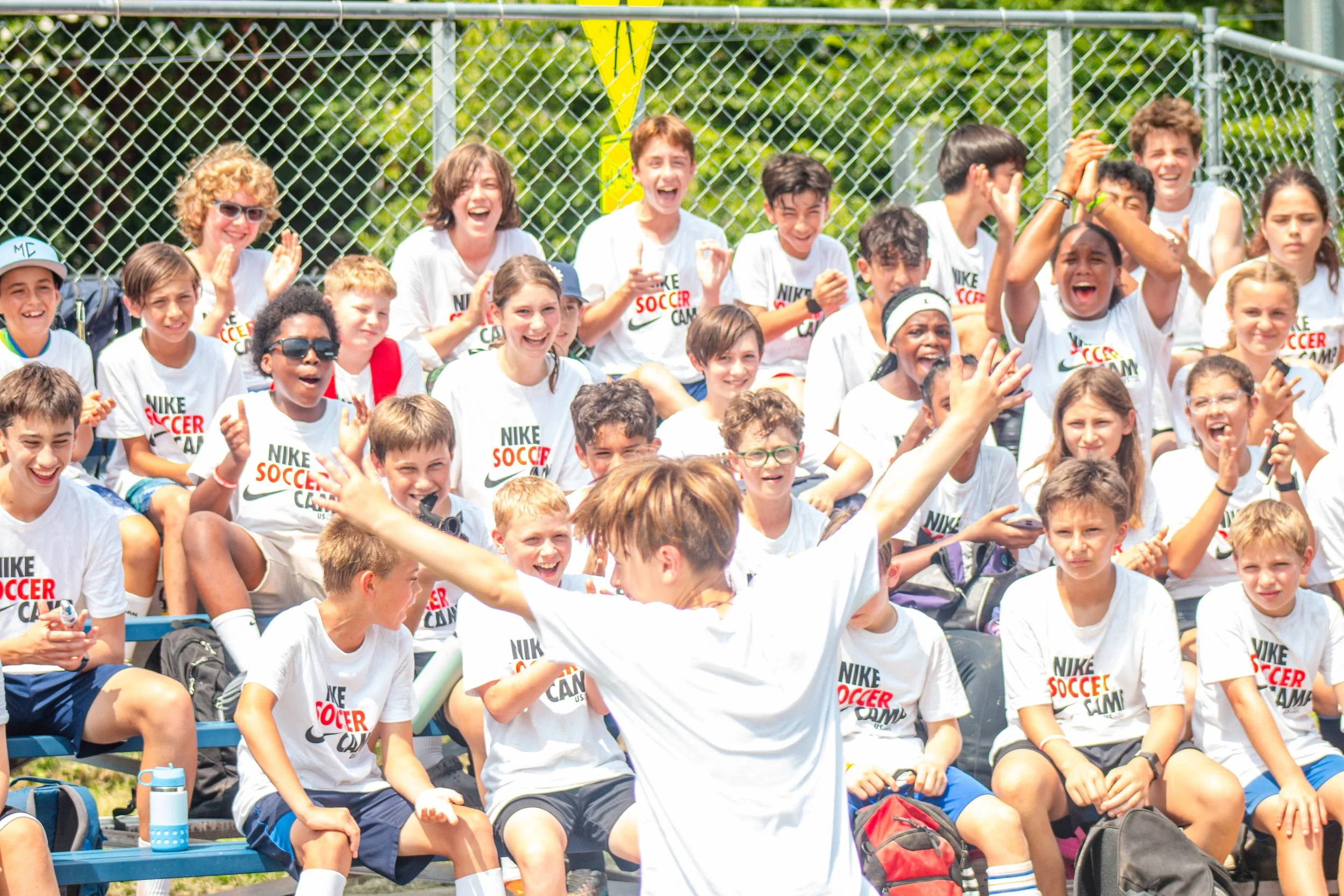 Group of young girls playing soccer on a field, with two girls in the foreground smiling and riding piggyback, others in the background