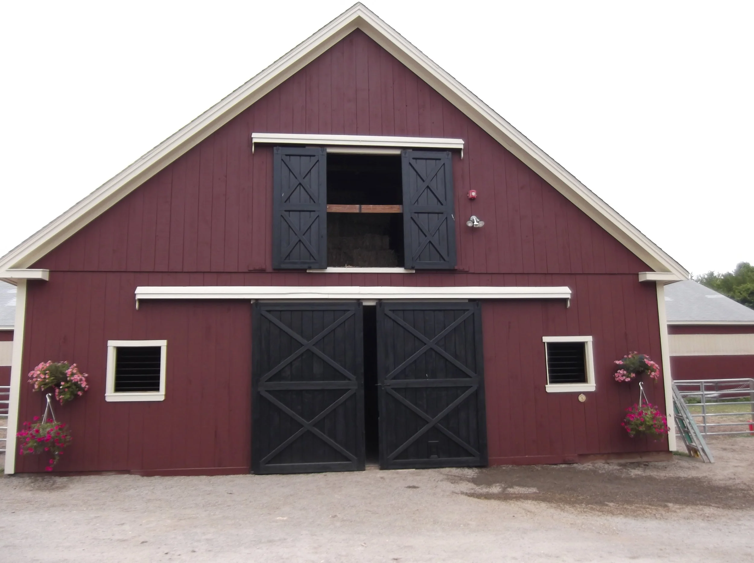  This is a photo of a stall barn that has eight 12’ x 12’ stalls, a 12’x12’ tack room, a 12’x12’ feed room and a full loft above. The barn is painted red with white trim and black doors. It has two large doors in front and two smaller windows on the 