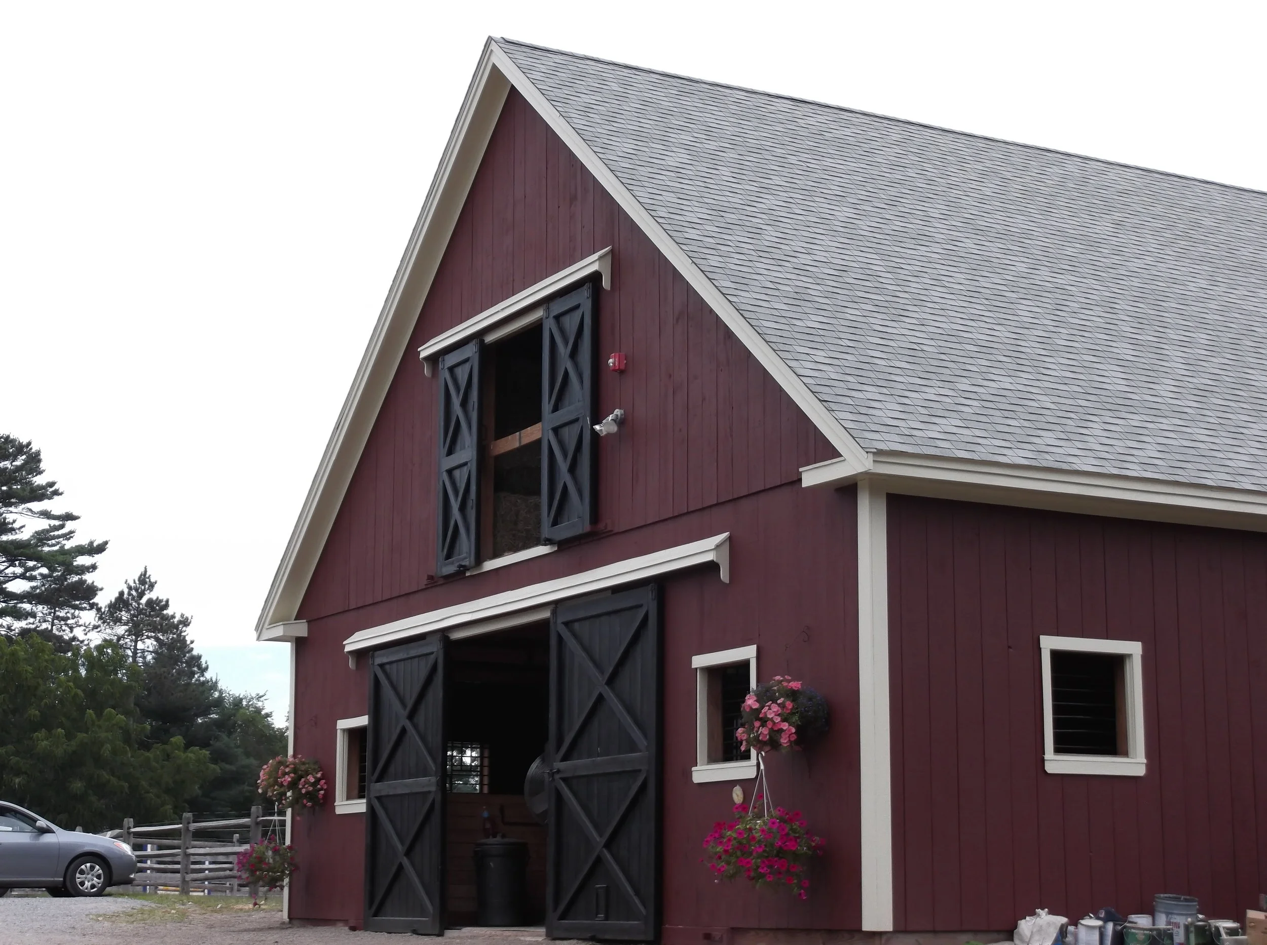  This is a photo of a stall barn that has eight 12’ x 12’ stalls, a 12’x12’ tack room, a 12’x12’ feed room and a full loft above. The barn is painted red with white trim and black doors. It has two large doors in front and two smaller windows on the 